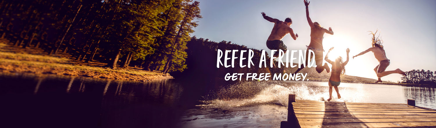 Four friends jump off a dock into a lake surrounded by evergreens on a summer evening. Text over the image reads Refer a Friend. Get Free Money.